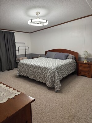 A bedroom with a bed, a nightstand, a lamp, a wooden dresser, and a ceiling fan.
