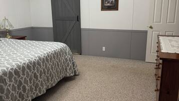 A bedroom with a bed, a dresser, a door, a wall-mounted picture, and a ceiling light fixture.