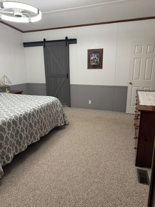 A bedroom with a bed, a dresser, a door, a wall-mounted picture, and a ceiling light fixture.