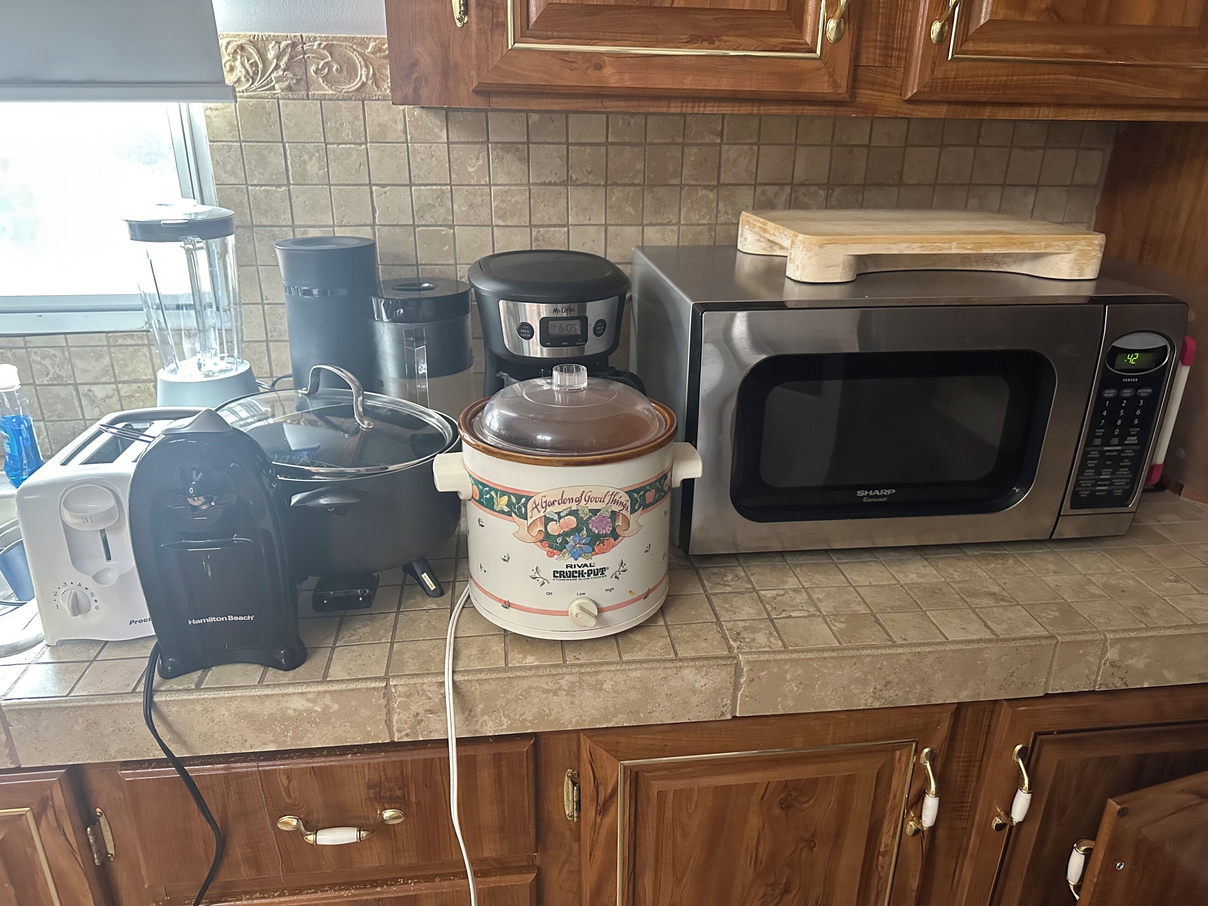 A kitchen with a microwave, toaster, slow cooker, and a coffee maker.