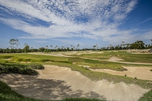 Camp de golf amb búnquers de sorra, cel serè i arbres al fons.