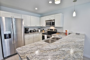 A modern kitchen with white cabinets, stainless steel appliances, granite countertops, and under-cabinet lighting.