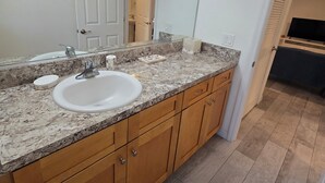 A bathroom with a white sink, wooden cabinets, a granite countertop, a large mirror, and a towel rack. - Luxurey-bedroom house in charming Homosassa with AC (Homosassa)