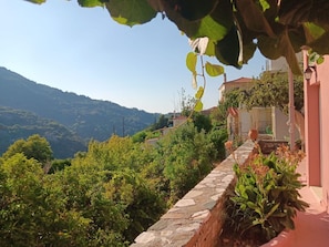 A stone pathway leading to a building with a red exterior, surrounded by lush greenery and hills in the background. - "House of Thalia" A Mediterranean home with soul and history (Manolates)