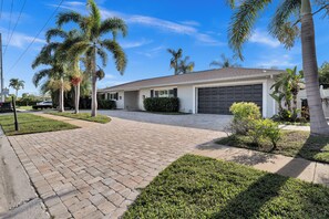 A residential property with a paved driveway, palm trees, and a garage. - Waterfront Pool Home • Hot Tub • Private Golf Field (Tampa)