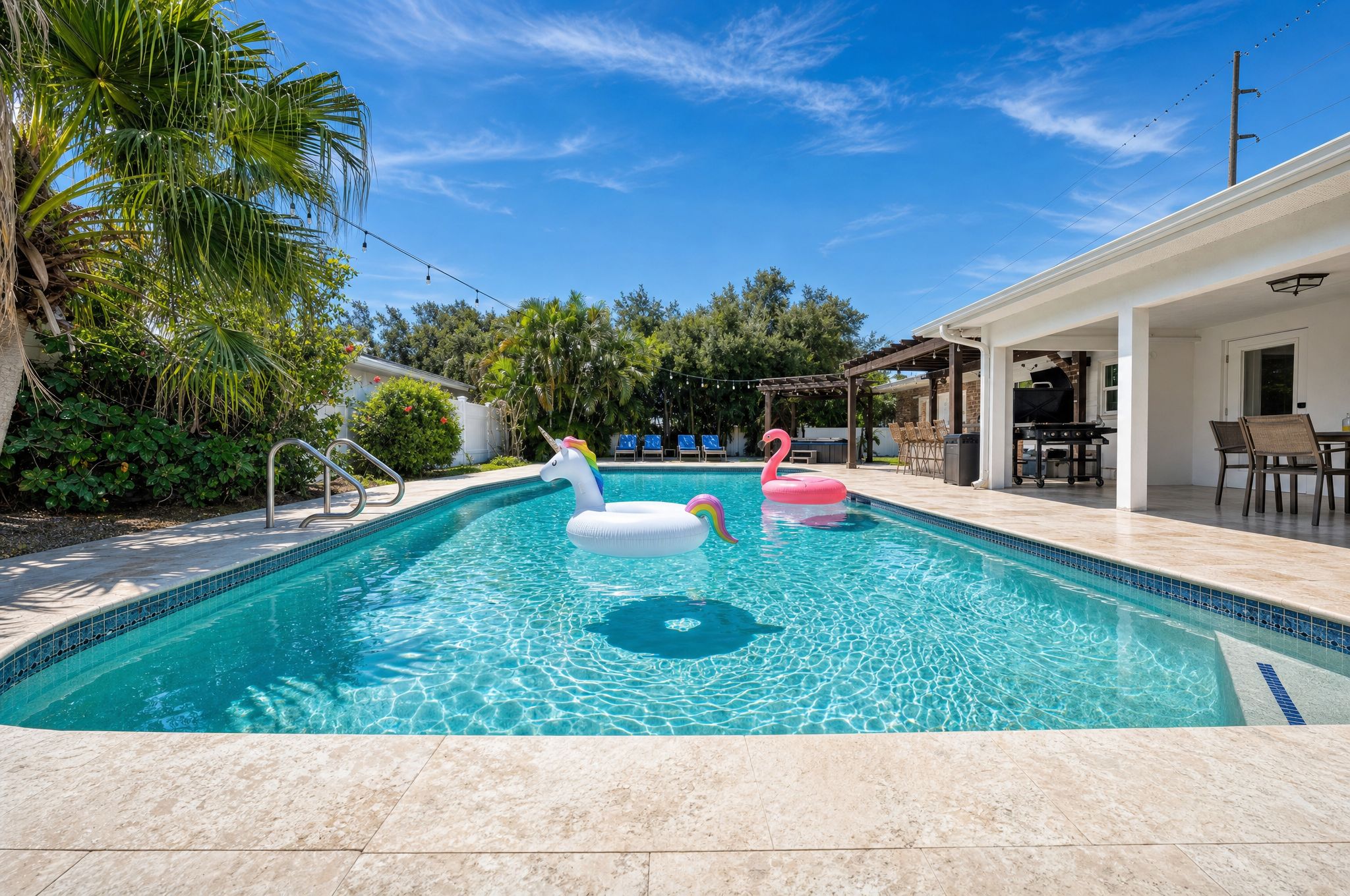 Ein Swimmingpool mit zwei aufblasbaren Einhorn- und Flamingoboots, umgeben von einer Terrasse mit Grill und Sitzgelegenheiten.