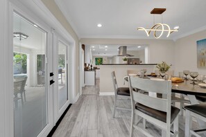 A modern kitchen with a central island, a dining area with a table set for four, and a hallway leading to a door. - Waterfront Pool Home • Hot Tub • Private Golf Field (Tampa)