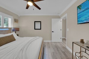 A bedroom with a bed, a ceiling fan, a door, and a wall-mounted TV. - Waterfront Pool Home • Hot Tub • Private Golf Field (Tampa)