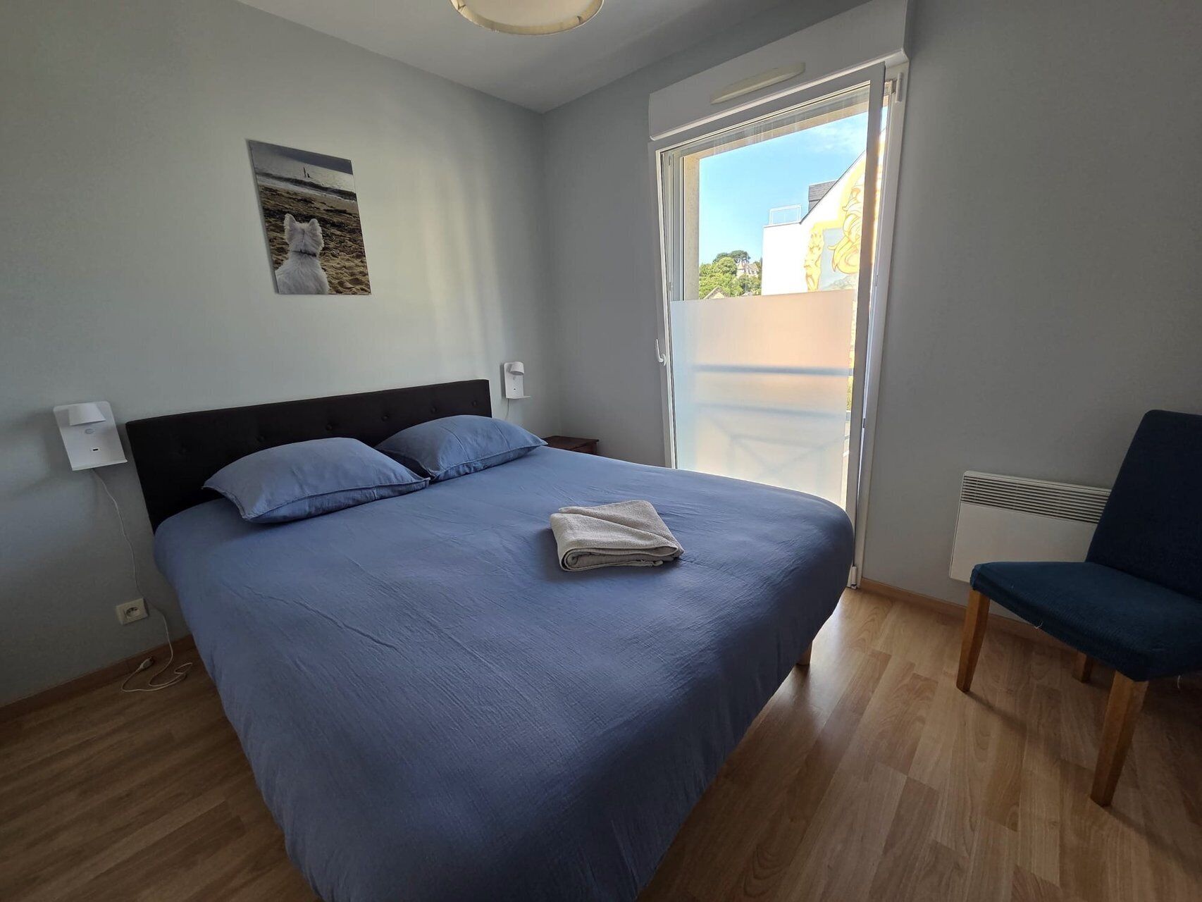 Une chambre à coucher avec un lit, une chaise, une fenêtre et un luminaire fixé au mur.
