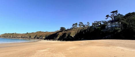 A beach with footprints, a clear sky, and a building on a hill.
