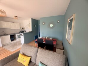 A compact living space with a kitchenette, dining area, and a sofa with a yellow pillow. - Le Primauguet ,Terrace ,50m from the beach (Saint-Cast-le-Guildo)