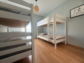 A room with bunk beds, a wooden floor, a hanging light fixture, and a framed picture on the wall. - Le Primauguet ,Terrace ,50m from the beach (Saint-Cast-le-Guildo)