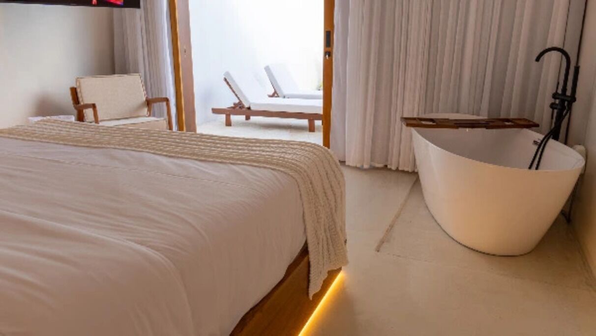 A bedroom with a large bed, a bathtub, and a view of the outside.