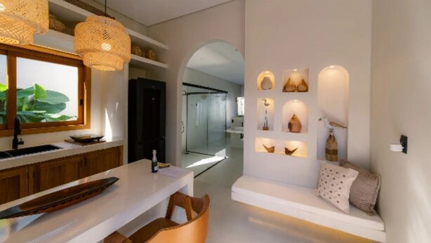 A modern kitchen with a dining area, a white sofa with cushions, and wall-mounted shelves with decorative items.