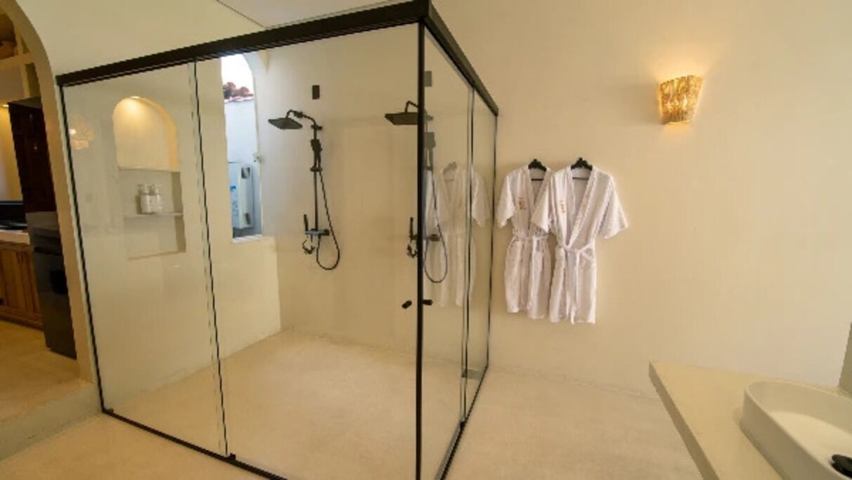 A glass-enclosed shower area with a handheld showerhead, a towel rack with white towels, and a wall-mounted light fixture.