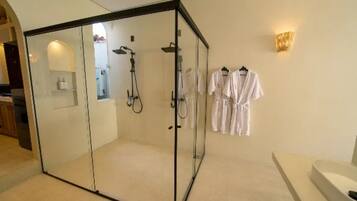 A glass-enclosed shower area with a handheld showerhead, a towel rack with white towels, and a wall-mounted light fixture.