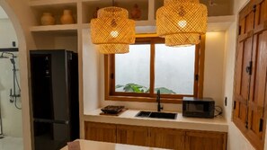 A kitchen with a black refrigerator, a microwave, and a window with a view of greenery.