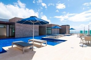 Ein Poolbereich auf dem Dach mit Liegestühlen und Sonnenschirmen, umgeben von modernen Gebäuden.