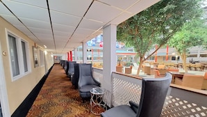 A hotel corridor with rows of seating, a patterned carpet, and a view of the outdoor seating area.