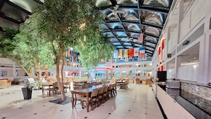 A spacious indoor atrium with multiple dining areas, a high ceiling with a glass structure, and various flags.