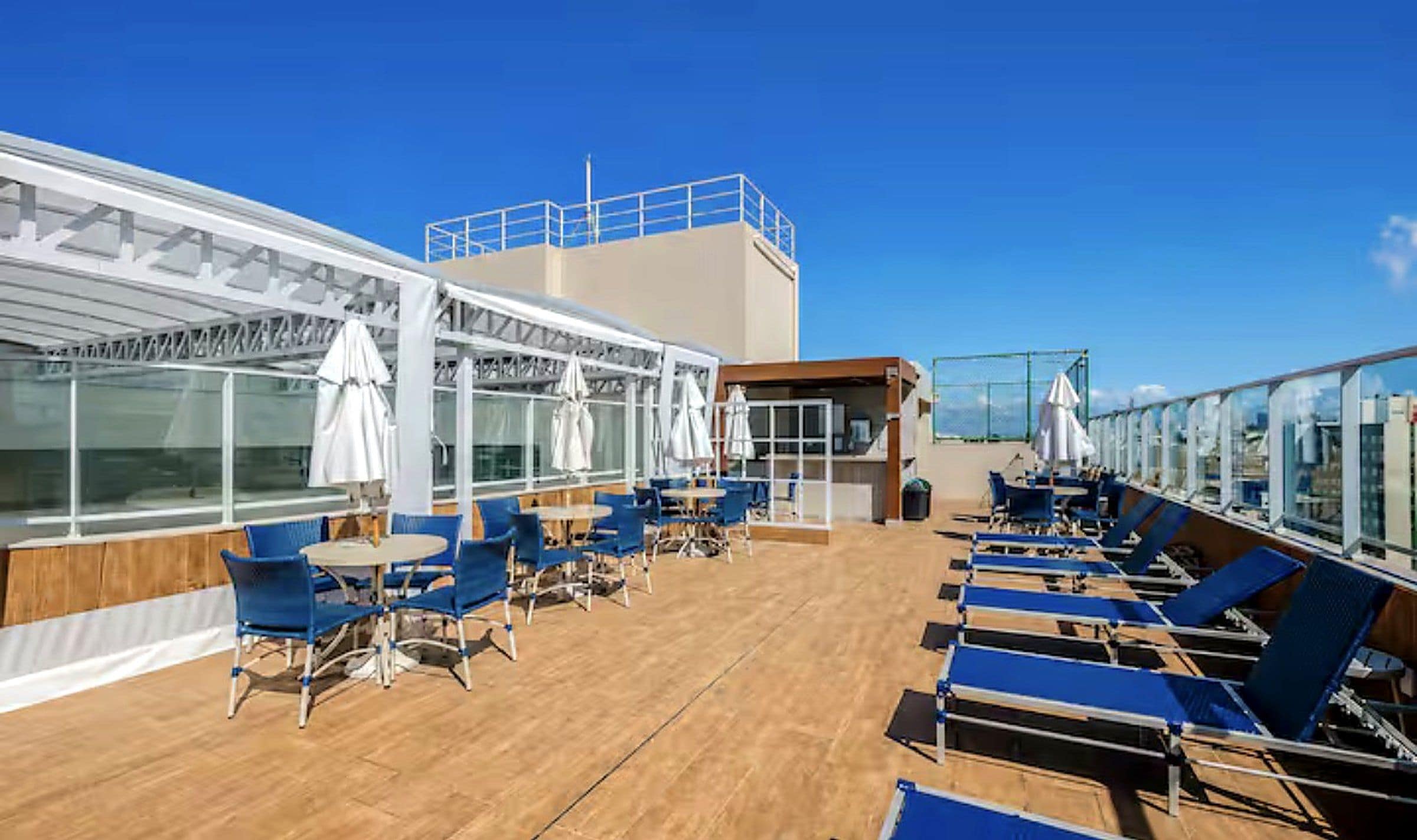 Een zonneterras met ligbedden en parasols, een overdekt zitgedeelte en een glazen balustrade.