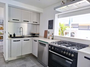 A modern kitchen with a gas stove, dishwasher, and a window with a view of the outdoors. - Villa Tartaruga - piscine privée, proche plage et centre ville (Sainte-Anne)