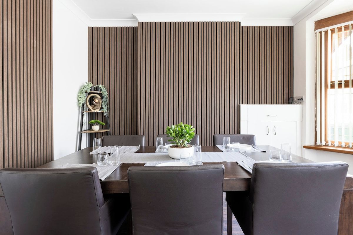 Een eetruimte met een lange tafel, donkere stoelen en verticale houten panelen aan de wanden.