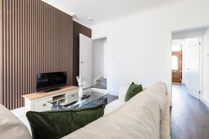 Een moderne woonkamer met een flatscreen televisie, een glazen salontafel en een bank met groene kussens.