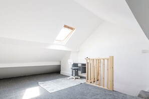 Een kamer met een schuine kap, dakraam, bureau, stoel en een houten afrastering.