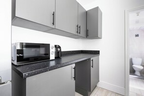 A compact kitchen with grey cabinets, a black countertop, and a microwave. - 46 Gladstone Street Walsall (Walsall)
