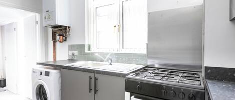 A compact kitchen with a washing machine, a gas stove, and an oven.