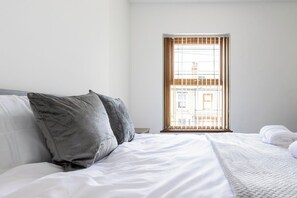 A hotel room with a bed, pillows, a window with blinds, and a view of buildings outside. - 46 Gladstone Street Walsall (Walsall)