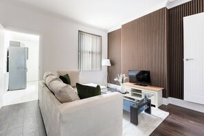A modern living room with a sofa, a glass coffee table, a flat-screen TV, and a wooden accent wall. - 46 Gladstone Street Walsall (Walsall)