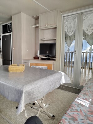 A modern kitchen with a built-in refrigerator, a flat-screen TV, and a dining area with a table and chairs. - Air-conditioned mobile home, on the edge of the beautiful La Coubre Forest (La Tremblade)