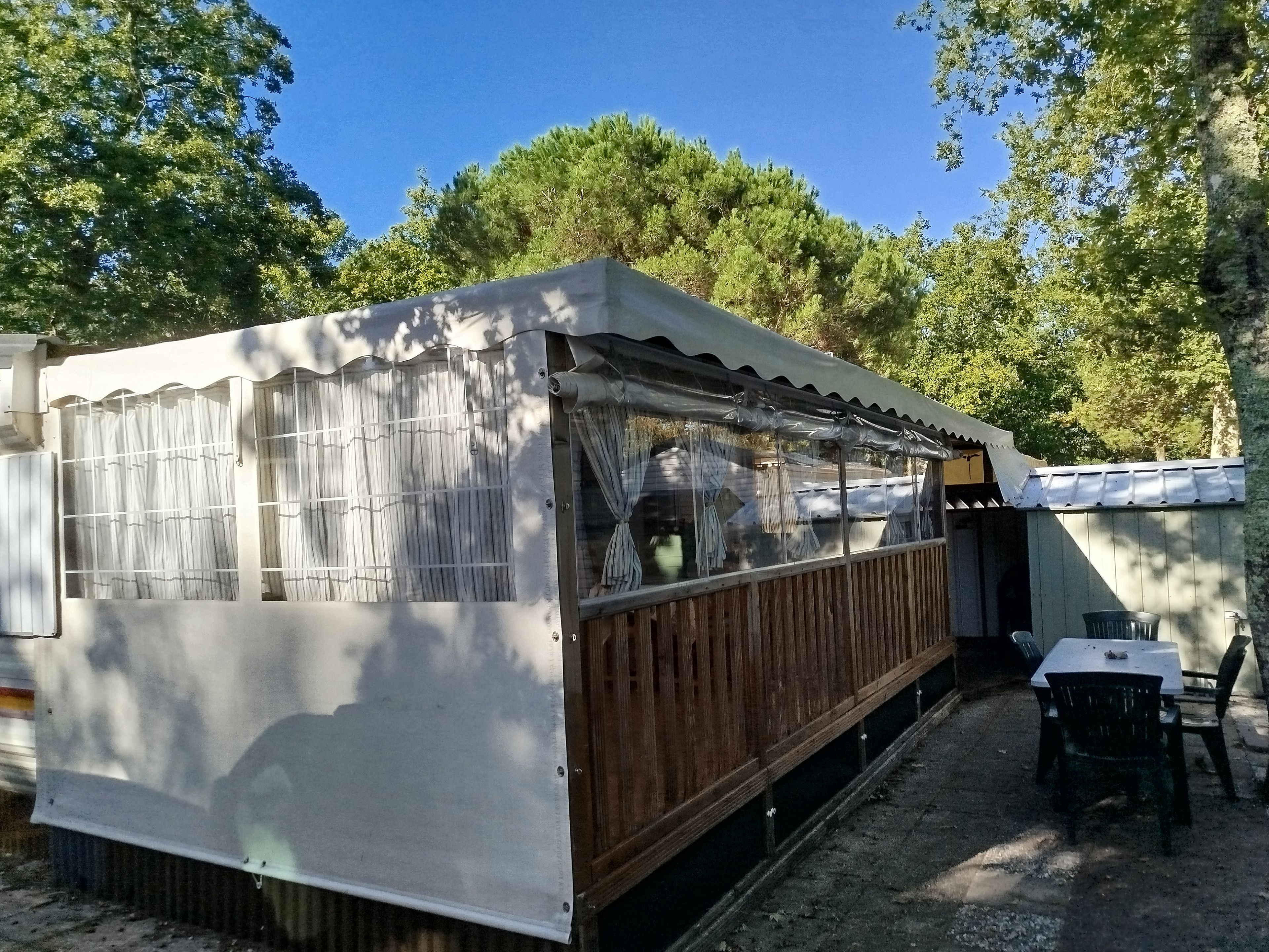 Un pequeño edificio de un solo piso con un patio techado, una terraza de madera y una mesa con sillas dispuestas en el exterior.