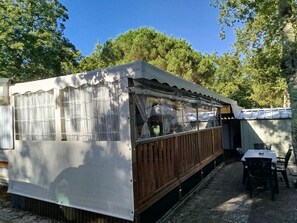 A small, single-story building with a covered patio area, a wooden deck, and a table and chairs set up outside. - Air-conditioned mobile home, on the edge of the beautiful La Coubre Forest (La Tremblade)