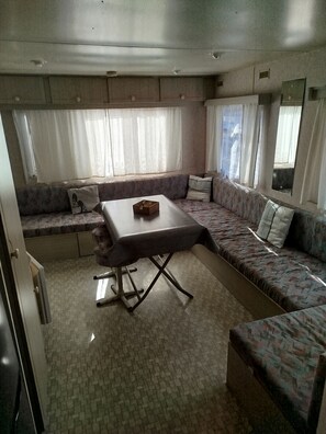 A compact living space with a sofa, a small table, and a kitchenette area. - Air-conditioned mobile home, on the edge of the beautiful La Coubre Forest (La Tremblade)