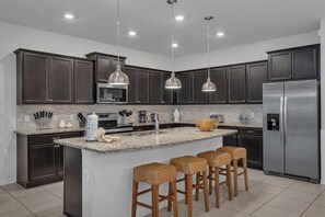 A modern kitchen with dark cabinets, stainless steel appliances, and a central island with bar stools. - Enchanted Escape Villa (Davenport)