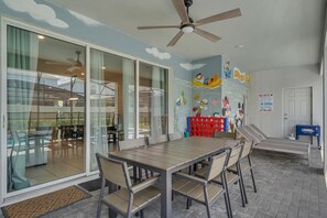 A dining area with a table and chairs, a ceiling fan, and a mural with cartoon characters. - Enchanted Escape Villa (Davenport)