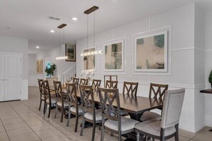 A dining area with a long table and multiple chairs, recessed lighting, and framed artwork on the walls. - Enchanted Escape Villa (Davenport)