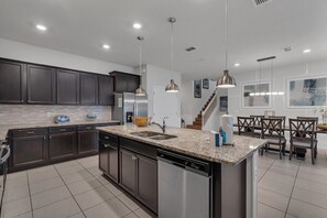 A modern kitchen with dark cabinets, granite countertops, stainless steel appliances, and pendant lighting. - Enchanted Escape Villa (Davenport)