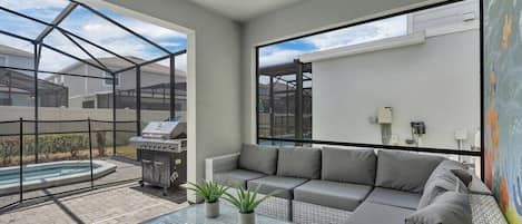 Un espacio exterior moderno con una mesa de centro de vidrio, sofá gris y una parrilla.