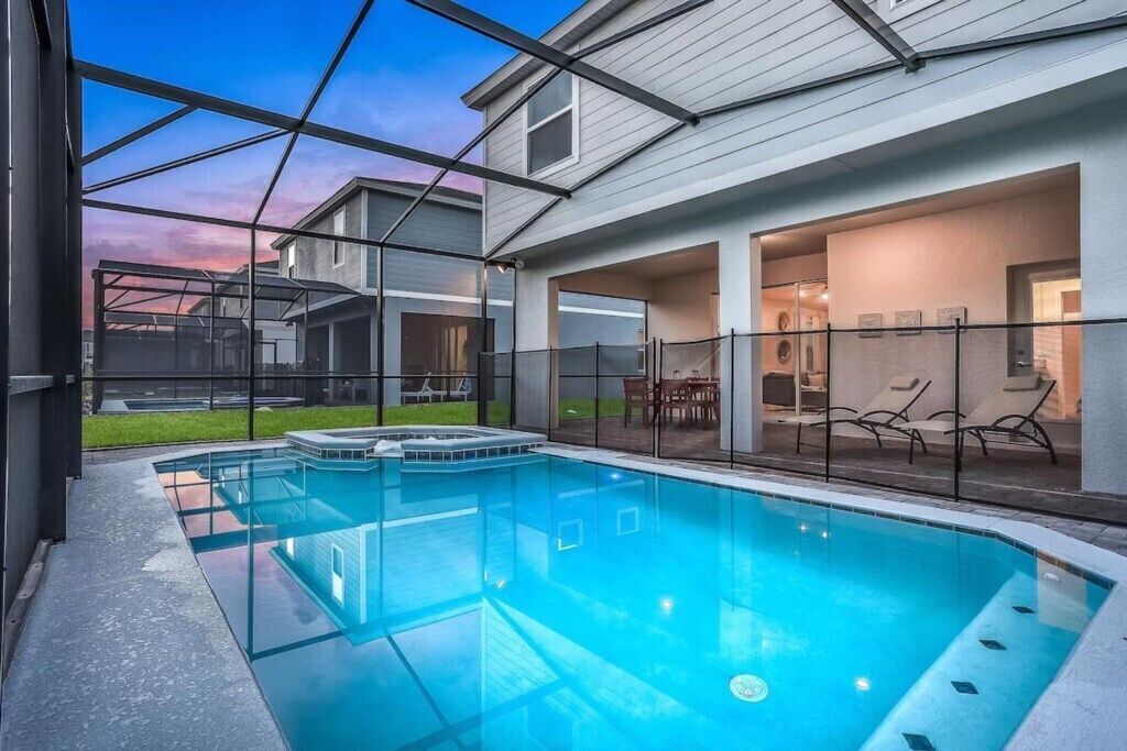Une piscine entourée de parois en verre, un espace patio avec des chaises et une vue sur un immeuble d’habitation.