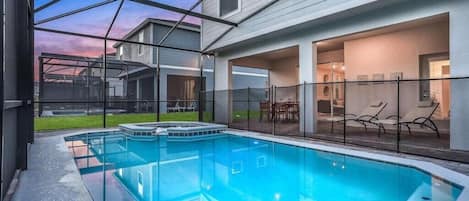 Una piscina con cerramiento de vidrio, un área de patio con sillas y vistas a un edificio residencial.