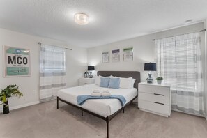 Une chambre d’hôtel avec un lit, des tables de chevet, une petite table, une lampe, une plante en pot et une fenêtre avec des rideaux.