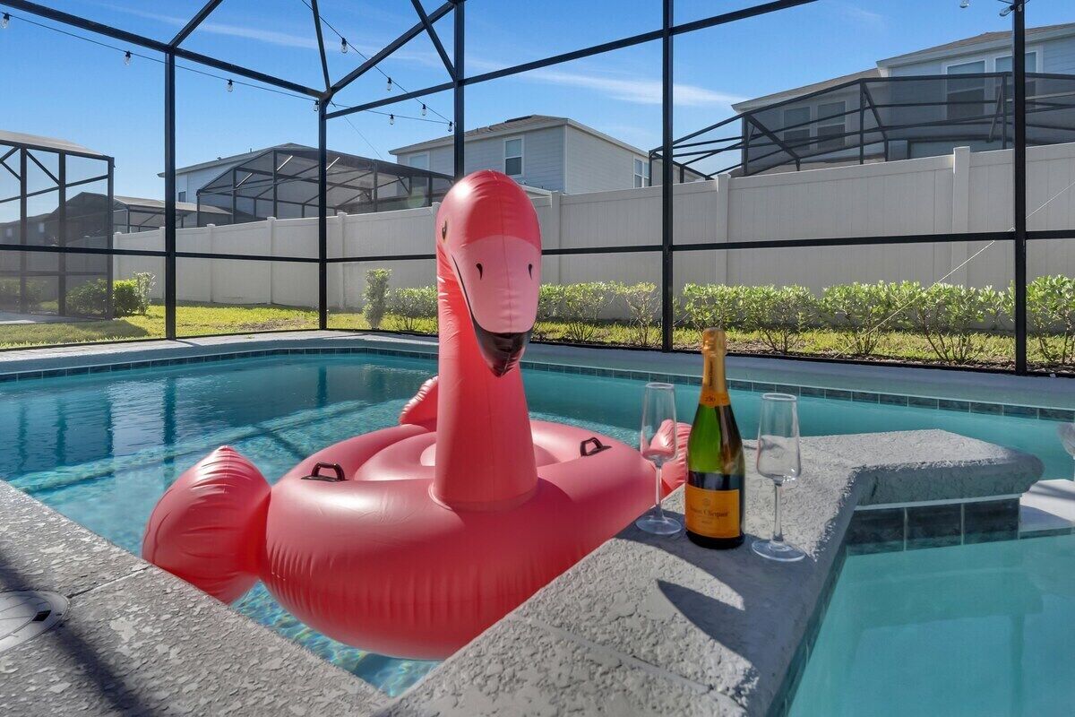 Una piscina con un flotador de flamenco inflable rosa, una botella de champán y una copa en el borde.