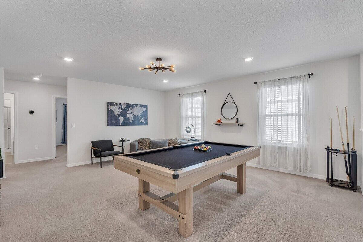 Una habitación con mesa de billar, sofá, sillón, una obra de arte con un mapa y un soporte para billar.