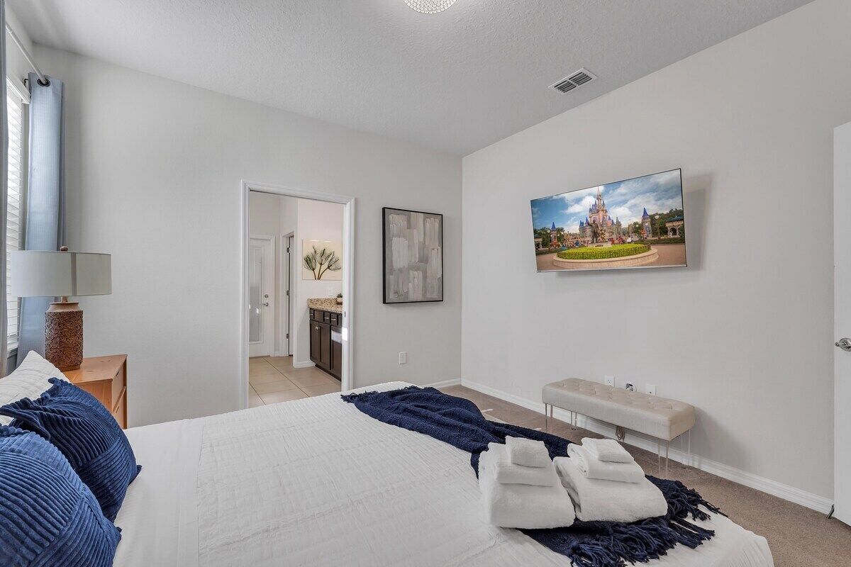 Een slaapkamer met een bed, een bankje, een televisie en een deur naar een badkamer.
