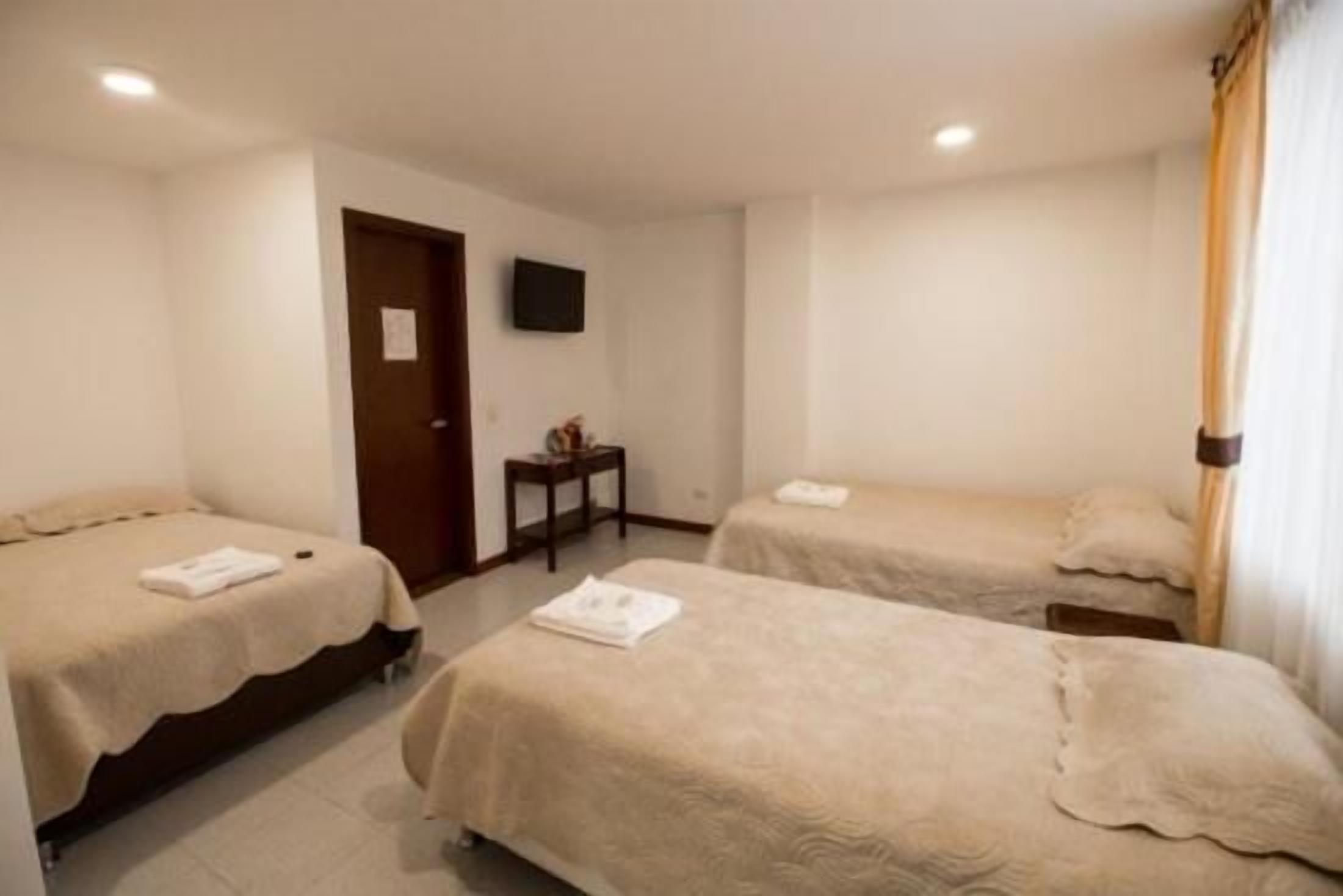 A hotel room with two single beds, a small table, a television, and a door.