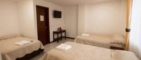 Une chambre d’hôtel avec deux lits simples, une petite table, un téléviseur et une porte.